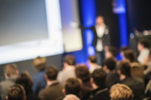 Photo of a person on stage giving a presentation to an audience.