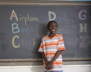 student smiles confidently by the school chalkboard