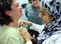 Using a shared stethoscope, med student Anila Chaudhary listens to patient Maria Aponte’s heart as internist Fernanda Porto Carreiro looks on. 