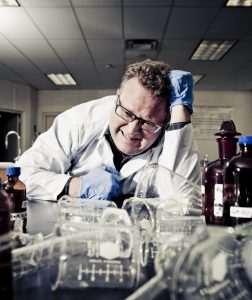 scientist in the lab is distressed while looking at overturned beakers 