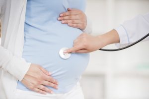 doctor examining a woman's pregnant belly with a stethescope