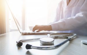 doctor using the computer with a stethoscope next to her