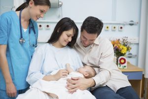 resident stands next to the bed while a couple cuddles their newborn