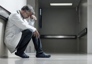 a stressed out doctor sits on the floor holding his head