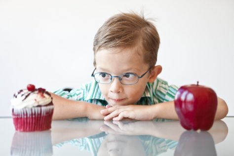boy stares at a cupcake that's placed next to an apple