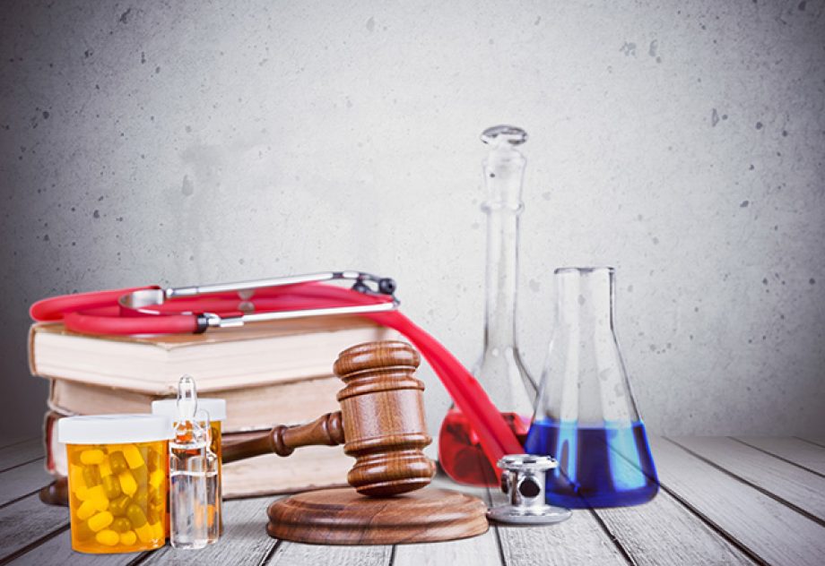 A pile of books and a wooden gavel are arranged on a table, along with medication bottles and lab beakers.