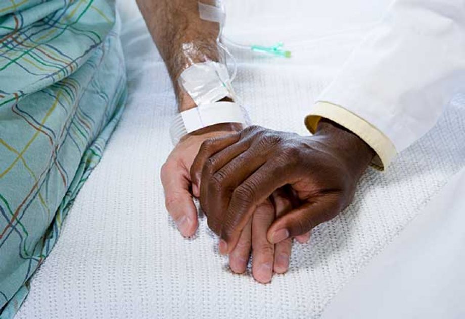 A doctor holds a patient's hand in a display of comfort.