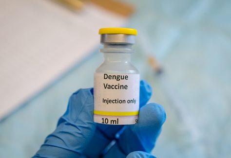 A gloved hand holds a dengue vaccine vial.