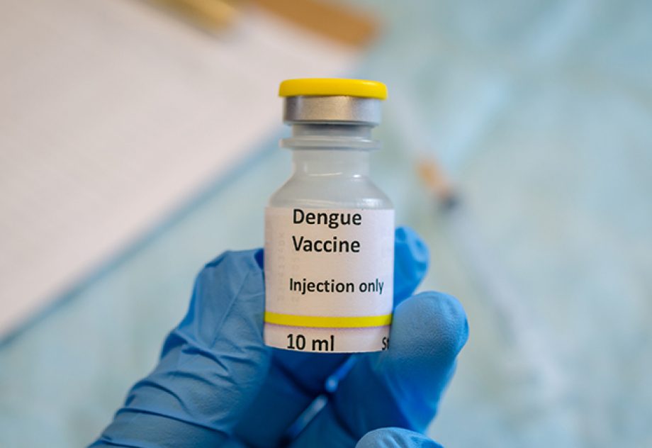 A gloved hand holds a dengue vaccine vial.