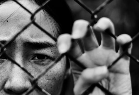 A young woman stands behind a chainlink fence.