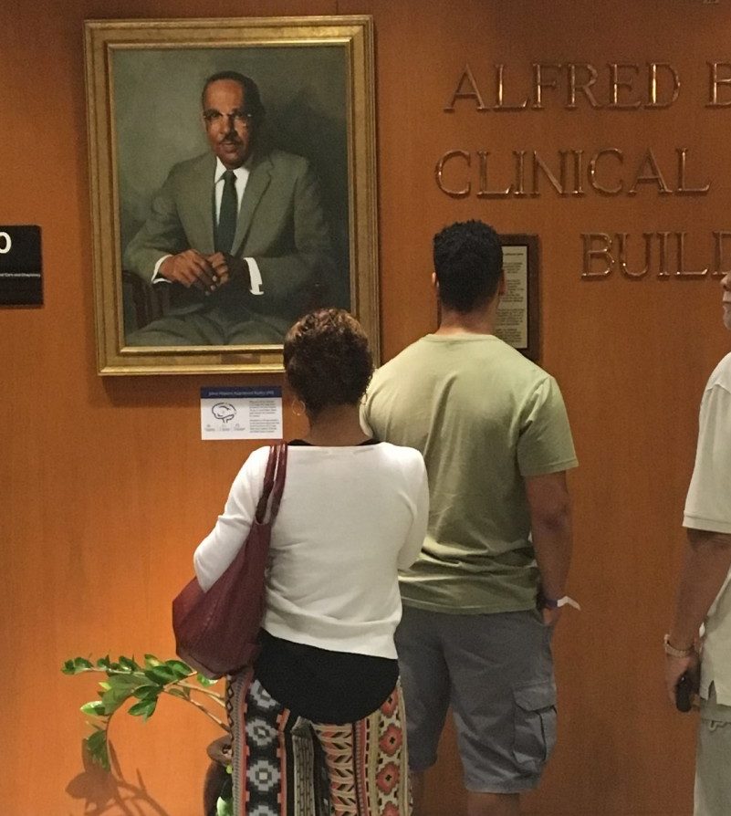 A family observes the portrait of Vivien Thomas.