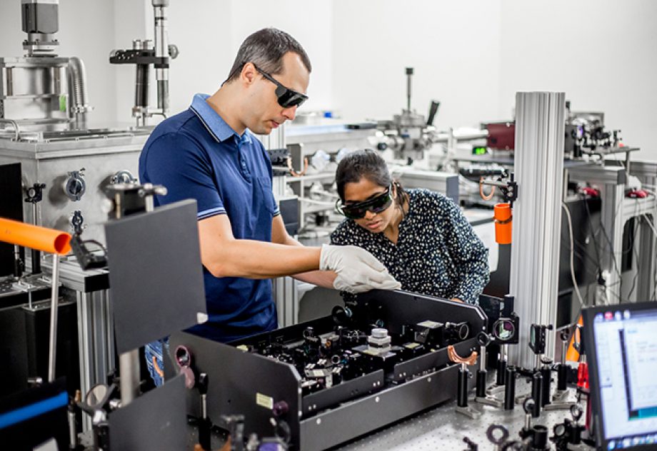 A mentor explains to a student how to use a high frequency laser for new materials research.