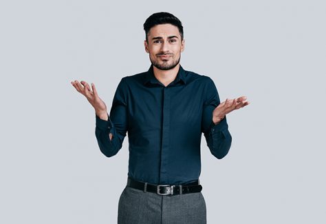 Confused young man shrugging shoulders and making face while standing against grey background