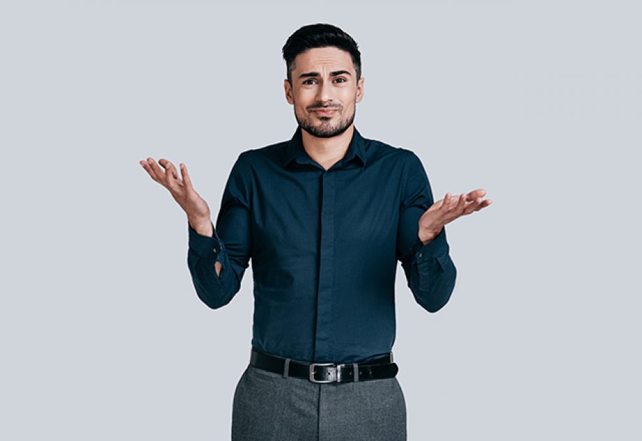 Confused young man shrugging shoulders and making face while standing against grey background