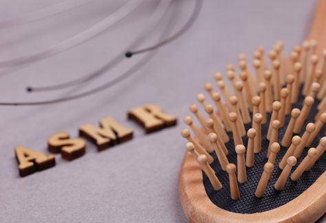 A hairbrush lies in the foreground; behind it are wooden letters spelling "ASMR."