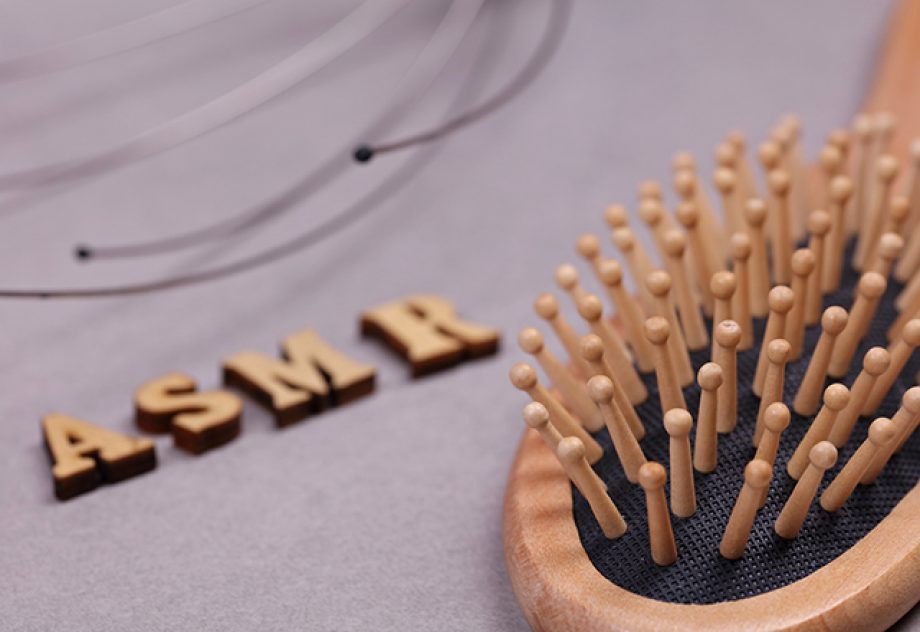 A hairbrush lies in the foreground; behind it are wooden letters spelling "ASMR."