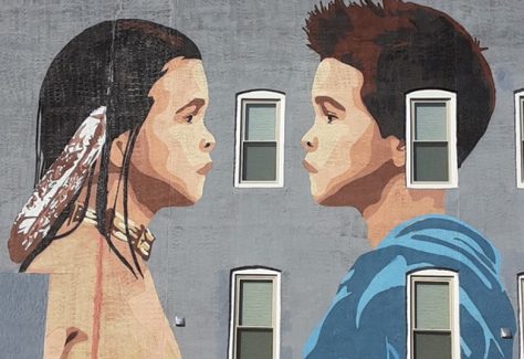 A mural of a Native American boy and a caucasian boy facing one another.