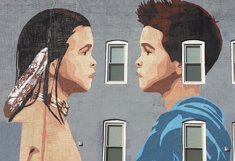 A mural of a Native American boy and a caucasian boy facing one another.