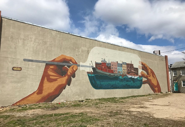 A large mural of two hands holding a ship in a bottle.