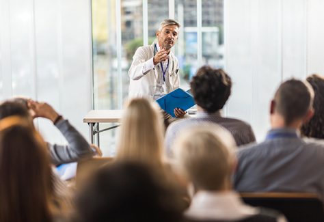 Male doctor talking to large group of people during a seminar in a board room.
