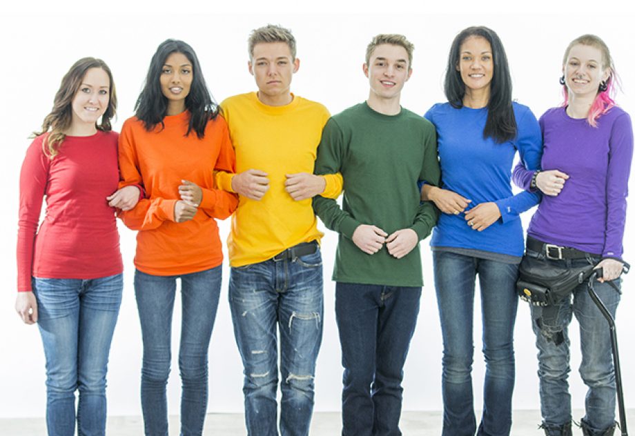 A multi-ethnic group of young people are standing in a row, with their arms linked together. They are wearing the colors of the rainbow for a gay pride concept.