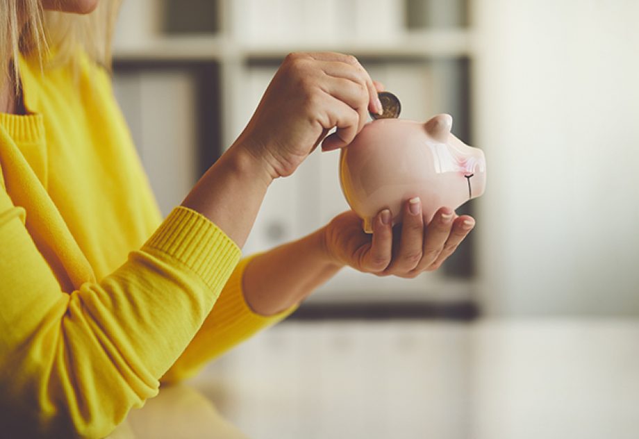 A woman inserts a coin into a piggy bank.