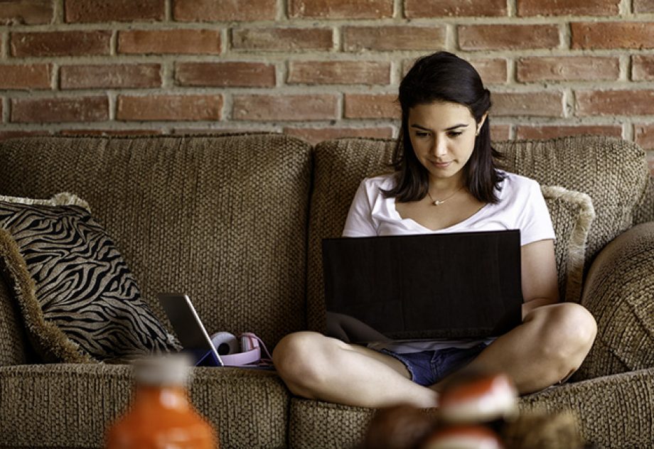 A young woman sits on the couch, using her laptop.