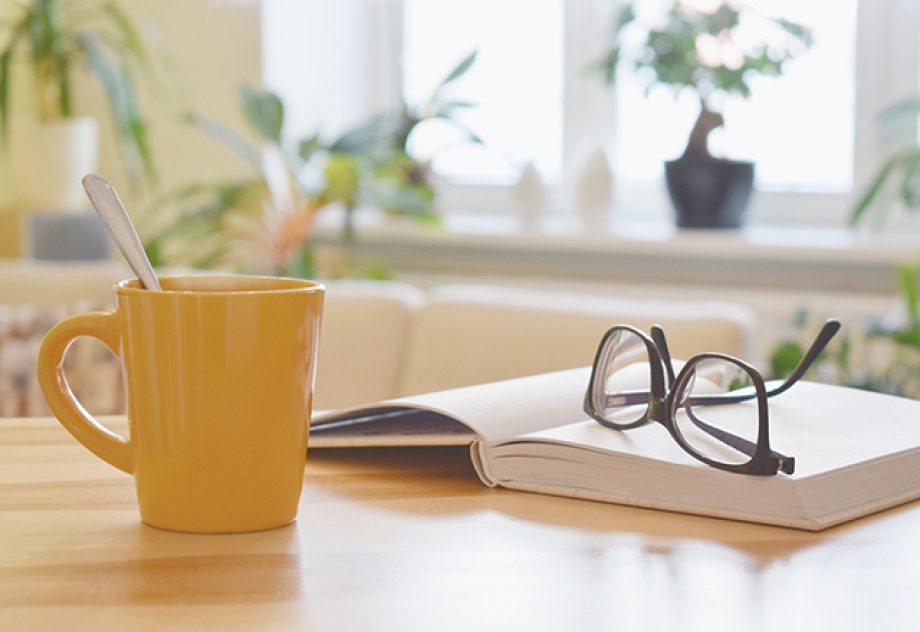 Yellow cup of tea, book and glasses on the table, cozy home interior background