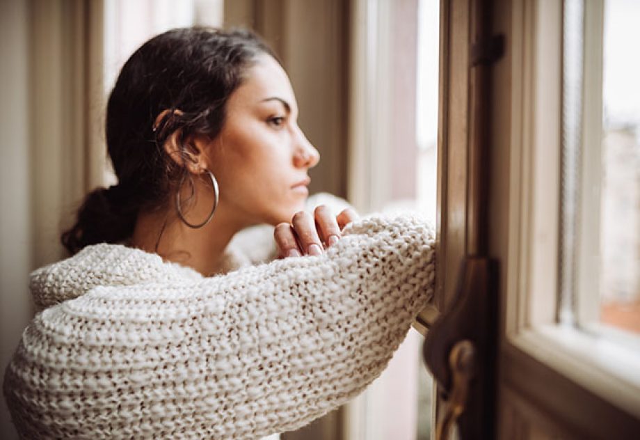 A pensive woman looks out of a window.