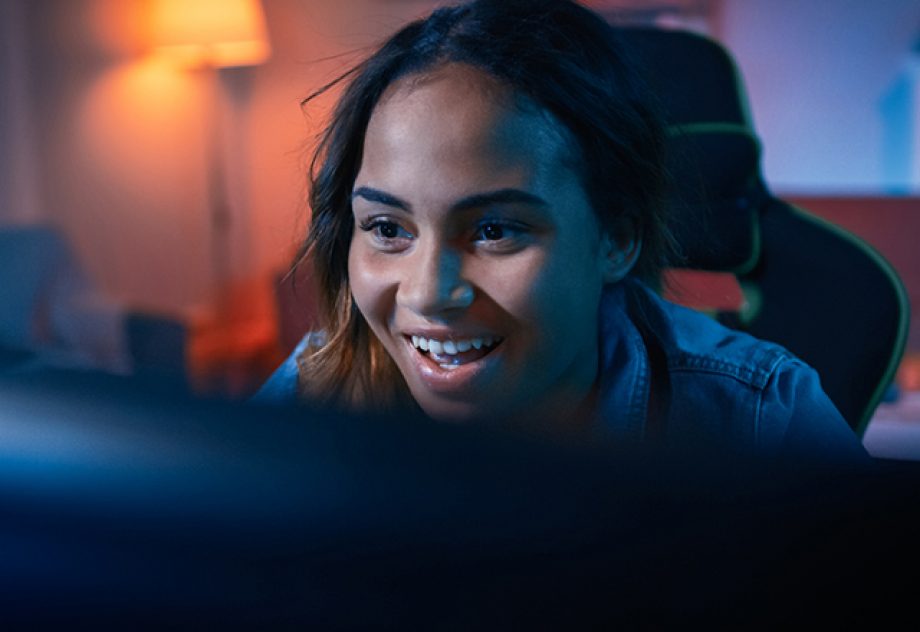 A young woman smiles while looking at her computer screen.