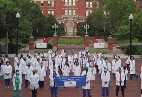 a group of Johns Hopkins doctors holding a sign that says " we stand with you".