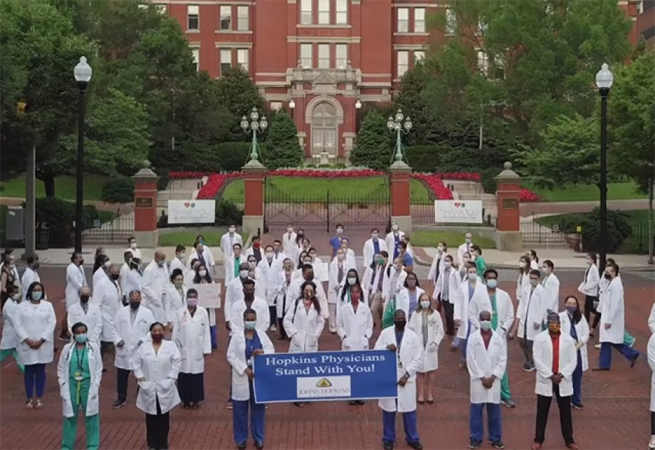 a group of Johns Hopkins doctors holding a sign that says " we stand with you".