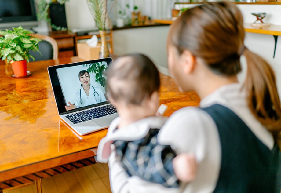 A mother with her baby is video calling a doctor on a laptop from home.