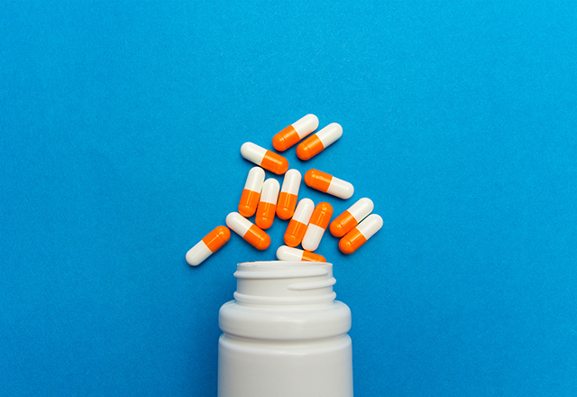 Orange white capsules (pills) were poured from a white bottle on a blue background. Medical background