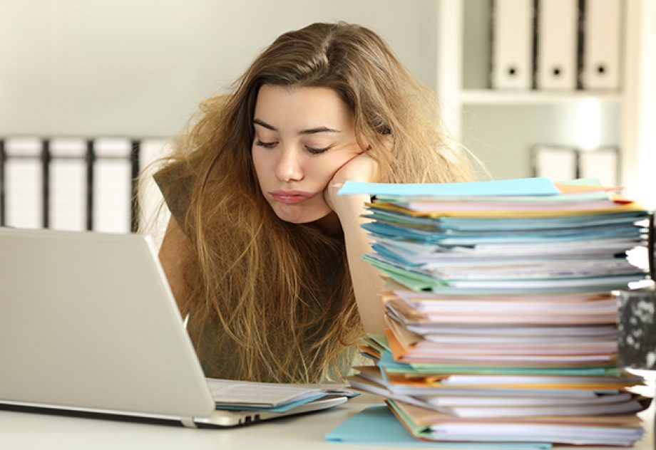 Exhausted young woman with tousled hair working hard reading a lot of documents at office.
