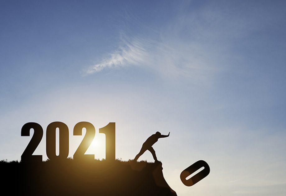 A man pushes the number zero off of a cliff; behind him is the number 2021 with a blue sky and sunrise.