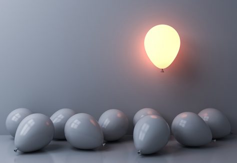 One balloon glows as it floats above other white balloons scattered along the floor in shadow.