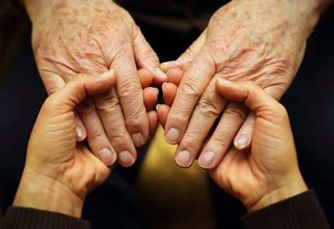 A pair of young hands hold a pair of older hands in a gesture of support.