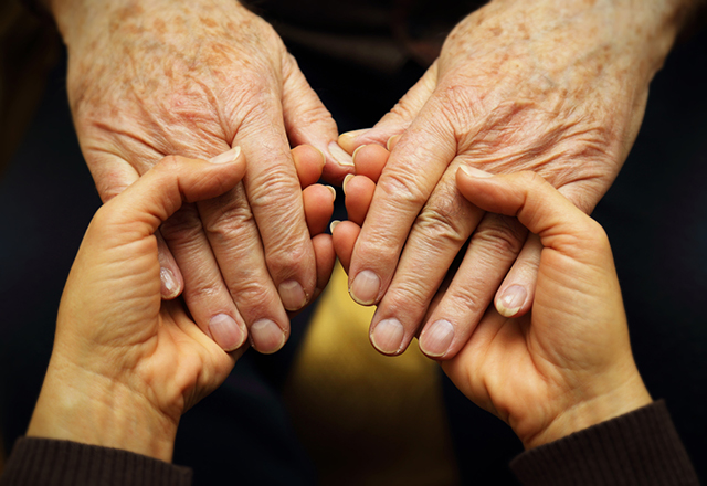 A pair of young hands hold a pair of older hands in a gesture of support.