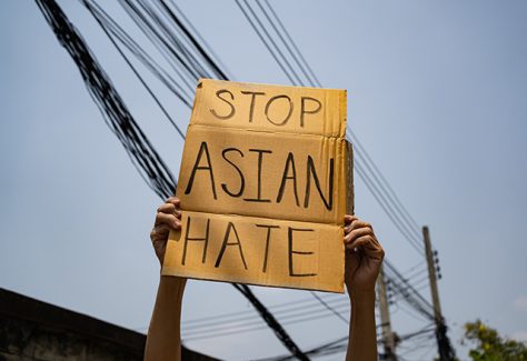 Two arms holding up a handmade sign that says "Stop Asian Hate."