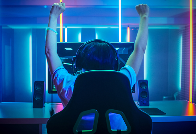 A gamer raises their arms in victory while seated at their computer.