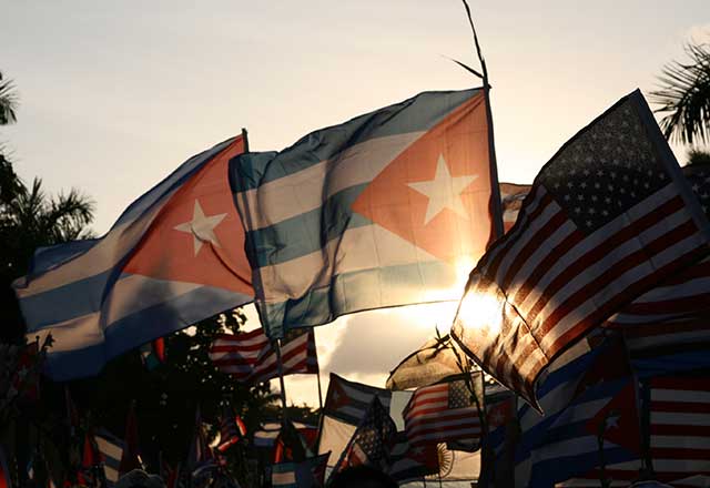 Cuban and American flags with a sunset in the distance