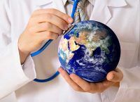 Doctor hold a stethoscope to a small globe.