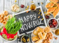 Happy Nowruz holiday background. Celebrating Nowruz sweets and treats- baklava, various dried fruits, nuts, seeds, wooden background with green grass.