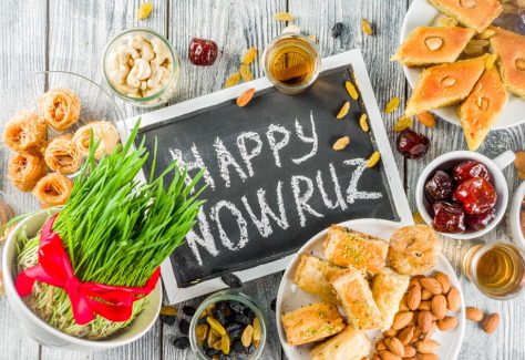 Happy Nowruz holiday background. Celebrating Nowruz sweets and treats- baklava, various dried fruits, nuts, seeds, wooden background with green grass.