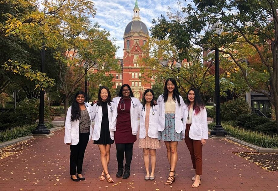 Friends in white coats stand on Johns Hopkins campus
