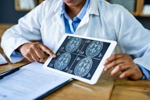 Neurosurgeon pointing to brain scan images on tablet.