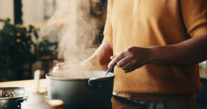 Cooking, hands and man in kitchen with pot, recipe and meal prep for dinner, lunch or supper. Home, stir and person by stove with ingredients, boiling and steam for nutrition, health and cuisine
