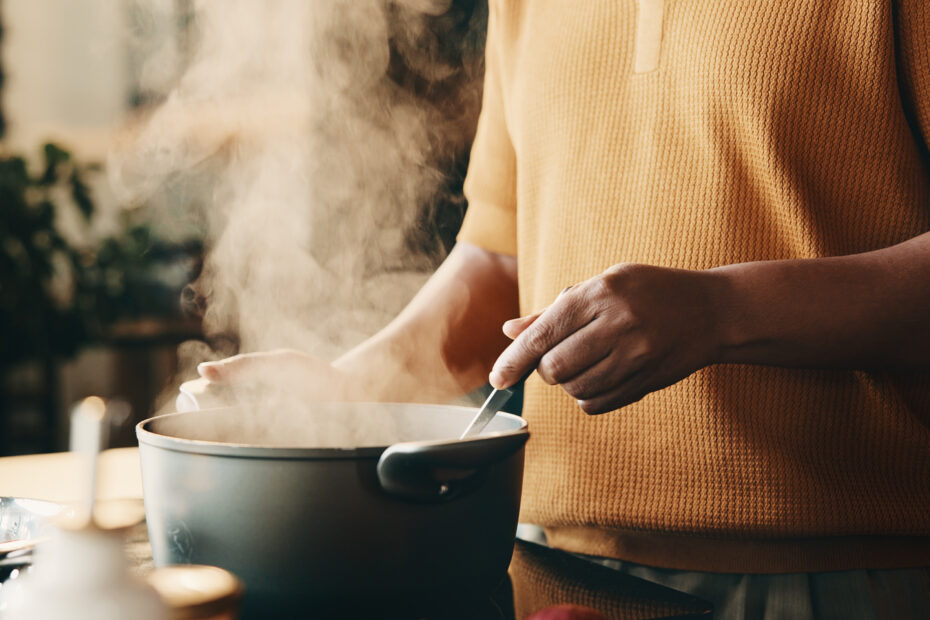 Cooking, hands and man in kitchen with pot, recipe and meal prep for dinner, lunch or supper. Home, stir and person by stove with ingredients, boiling and steam for nutrition, health and cuisine